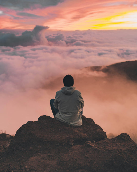 A calm person, in the mountains, above the clouds, feeling a sense of peace looking above it all.